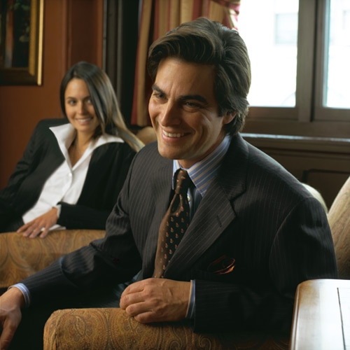 A smiling man seated in an armchair wearing a suit.